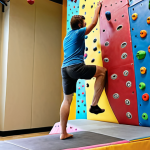 **Beginner indoor climbing gym:** A person learning basic climbing techniques on a colorful indoor climbing wall, with an instructor nearby providing guidance. Focus on proper hand grip and foot placement.